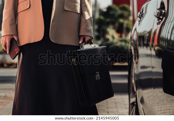 Unrecognisable Elegant Business Woman with\
Briefcase and Smartphone Standing Near the\
Car