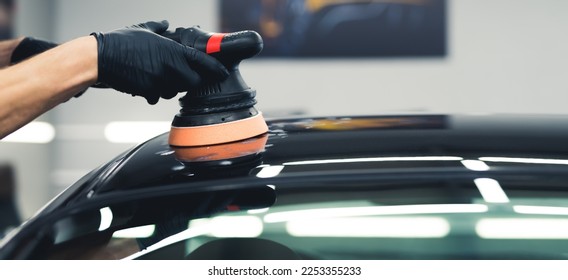 Unrecognisable man hands in black gloves holding professional buffer tool polishing paintjob on top of black car. Car detailing process. Horizontal indoor shot. High quality photo