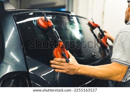 Unrecognisable man instaling rear window pane in the back of car using professional tools. Car maintenance. Garage work. Horizontal indoor shot. High quality photo