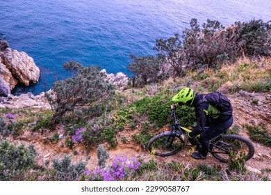 Unrecognisable mountain biker descends on a challenging trail steep towards the sea, Finale Ligure, Italy
