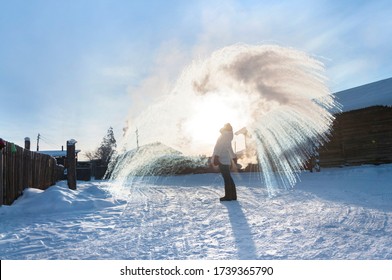 Unrecognisable Person Pouring Hot Water Up In The Sky, Sunny Winter Day In Oymyakon, Yakutia. Boiling Water Challenge, Which Instantly Freezes, Turns Into Snow If The Temperature Is Extremely Cold