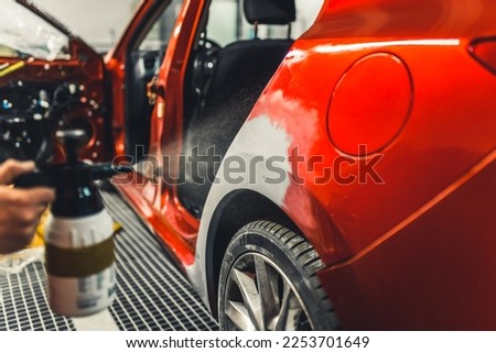 Unrecognisable person removing dent from body of red car using putty. Professional tools. Car maintenance. Horizontal indoor close-up shot. High quality photo