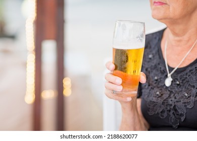 Unrecognisable Senior woman sitting at a table in a summer cafe and drinking beer from a tall glass