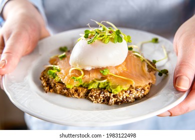 Unrecognisable Woman In Blue Shirt Holds A Plate With Salmon Toast, Avocado And Posched Egg. Close Up. Healthy Vegetarian Breakfast Food. Brain Food Concept.