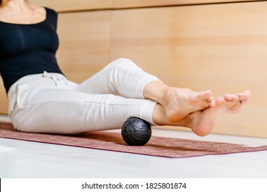 Unrecognisable woman using massage ball for muscle soreness after fitness exercise, muscle strain after high-intensity workouts, and physical and mental exertion after sitting in the office.