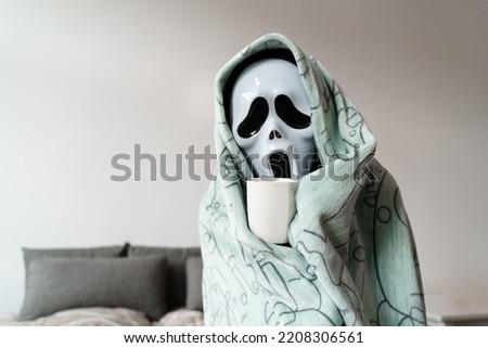 Unrecognised person in ghost sad mask in plaid freezing at home. Cold Halloween at home. Energy crisis 