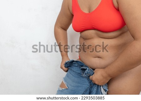 Unrecognizable adipose, fat, obese and overweight woman in red bikini pulling and getting dressed in small size tight jeans, to fit hips in clothes on white background. Preparation summer season