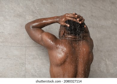 Unrecognizable African American Guy Taking Shower And Washing Head Standing Back To Camera Under Falling Water In Bathroom At Home. Haircare And Bodycare. Rear View Shot