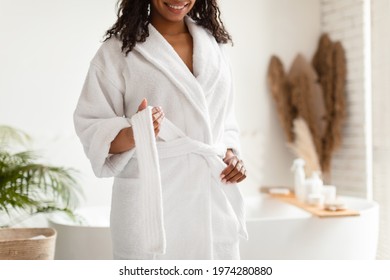 Unrecognizable African American Lady Untying White Bathrobe Preparing For Beauty Ritual Standing In Modern Bathroom In Hotel Spa Center. Female Beauty And Body Care. Cropped