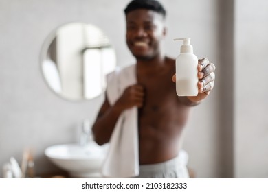 Unrecognizable African American Man Showing Hands Sanitizer Or Liquid Soap Bottle To Camera Standing In Modern Bathroom At Home. Selective Focus On Hygiene Product. Shallow Depth