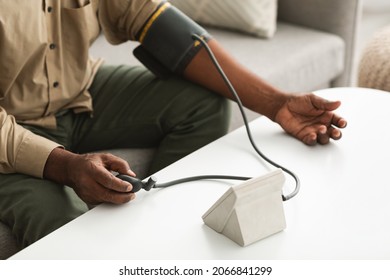 Unrecognizable African American Man Using Blood Pressure Cuff Device Measuring Arterial Tension Feeling Unwell At Home. Cropped Shot Of Male Having Hypertension. Health Problems In Older Age