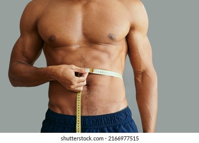 Unrecognizable African American muscular build man measuring his waist with tape measure.