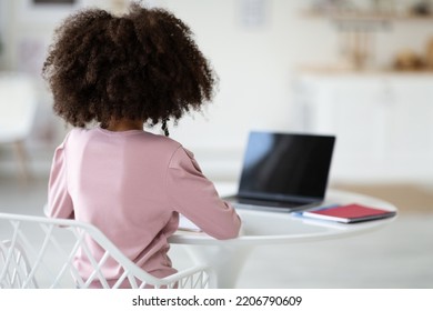 Unrecognizable african american school girl sitting at desk at home, using laptop with black blank screen, having video lesson, mockup, back view, copy space. Home-schooling concept - Powered by Shutterstock