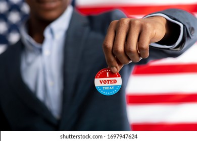 Unrecognizable african citizen of America holds I voted today button, typical of US elections on American flag.
