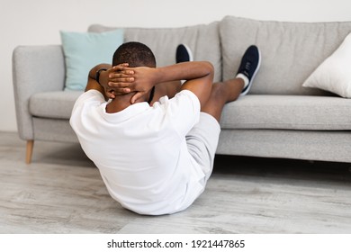Unrecognizable African Man Doing Abs Crunches With Legs On Couch Working Out Back To Camera At Home. Domestic Fitness Workout And Modern Sporty Lifestyle Concept. Rear View