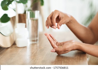 Unrecognizable African Woman Taking Beauty Supplements For Glowing Skin, Holding Omega-3 Fish Oil Capsules In Hands, Side View