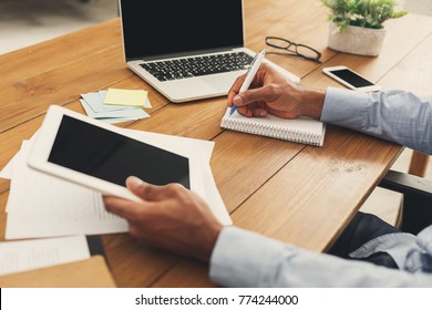 Unrecognizable african-american businessman working on digital tablet and writing in notebook in modern office, side view, copy space - Shutterstock ID 774244000