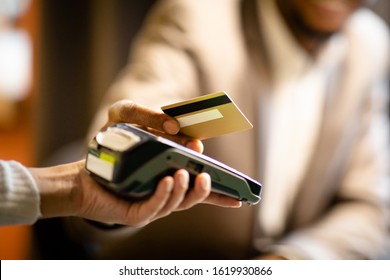 Unrecognizable afro businessman in suit giving credit card to barman paying with gold credit card in cafe, close up