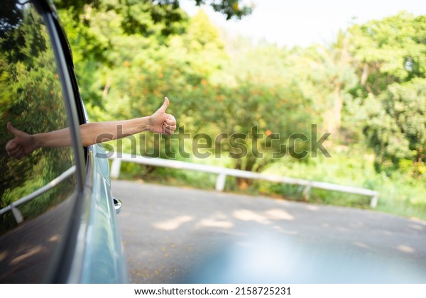 Unrecognizable Asian woman driver showing a\
thumb up outside the vehicle while driving a car. Happy woman\
driver or passenger showing her thumb up during in the car. Safety\
trip and freedom\
concept.