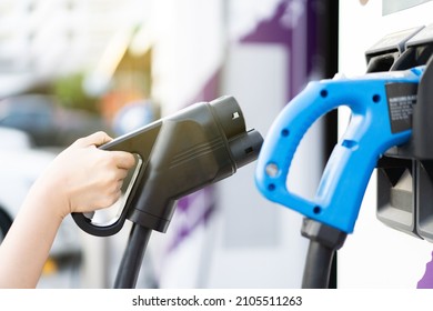 Unrecognizable Asian woman holding a DC - CCS type 2 EV charging connector at EV charging station, woman preparing an EV - electric vehicle charging connector for recharge a vehicle.