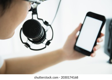 Unrecognizable Asian Young Man Making A Home Podcast Or Online Radio Live Streming And Looking At His Smartphone. Mockup Empty Blank Screen Smartphone.