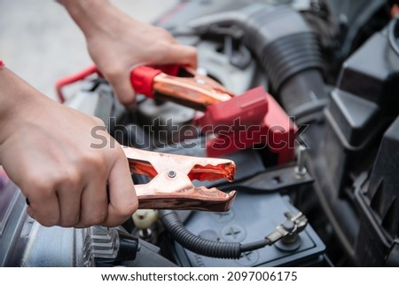 Unrecognizable Asian young woman trying to jumping a vehicle battery cable from other car close up, a car run out of battery. Emergency car broken situation.