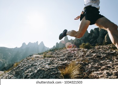 Unrecognizable athlete or sports enthusiast with strong legs with muscles runs through hard terrain mountain path on ultra trail marathon training or race, beautiful natural park scenery