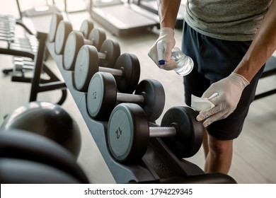 Unrecognizable Athlete Spraying Dumbbells With Disinfectant In A Health Club. 