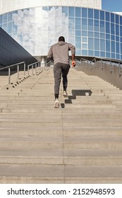 Unrecognizable Athletic Black Man Running Up Concrete Stairs Towards Modern Business Center While Having Outdoor Workout, Low Angle Rear View