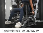 Unrecognizable athletic woman exercising her legs on abductor machine at gym