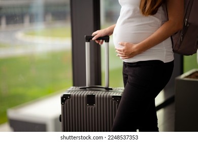Unrecognizable attractive caucasian brunette young pregnant woman,tourist on holiday with suitcase, backpack in airport station.Travelling by plane, flying during active pregnancy. - Shutterstock ID 2248537353