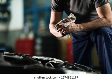 Unrecognizable auto mechanic cleaning his dirty hands after repairing car engine in a workshop. 