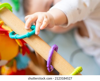 Unrecognizable Baby Boy Reaching For A Toy In Crib. Newborn Playing In Bed, Exploring And Developing Toys. Child Curiosity And Parenting Concept. Blurry Background