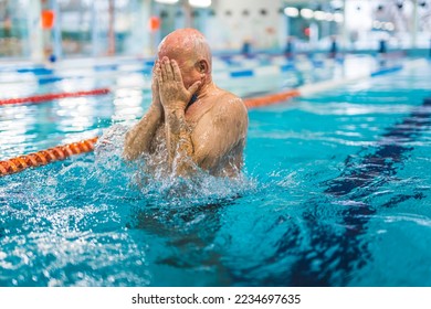 Unrecognizable bald caucasian senior adult man in a swimming pool covering his face with both hands. Leisure time activities. Active seniors. High quality photo - Powered by Shutterstock