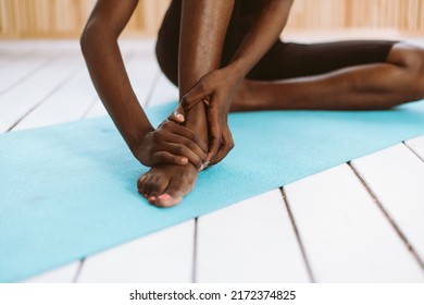 Unrecognizable Barefoot Dark Skin Multiracial Woman Holding And Touching Feet. Stretching And Doing Yoga Exercises On Blue Mat In Gym. Female Feeling Pain In Stiff Joints Of Foot Ligaments And Tendons