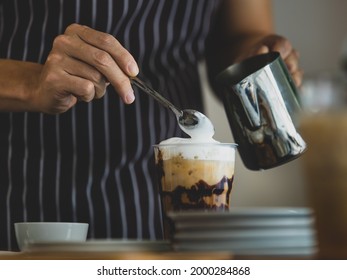 Unrecognizable  Barista Using Spoon To Gentle Topping Glass Of Sweet Coffee At Bar Counter With White Milk Froth From Metal Jar To Enhance Taste Of Softness And Mellowness