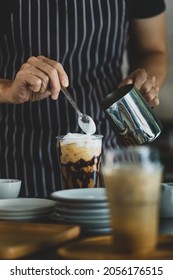 Unrecognizable  Barista Using Spoon To Gentle Topping Glass Of Sweet Coffee At Bar Counter With White Milk Froth From Metal Jar To Enhance Taste Of Softness And Mellowness