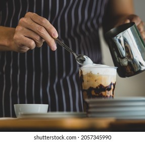 Unrecognizable  Barista Using Spoon To Gentle Topping Glass Of Sweet Coffee At Bar Counter With White Milk Froth From Metal Jar To Enhance Taste Of Softness And Mellowness