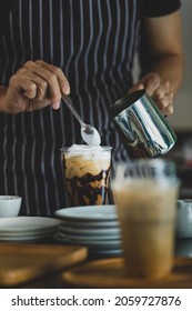 Unrecognizable  Barista Using Spoon To Gentle Topping Glass Of Sweet Coffee At Bar Counter With White Milk Froth From Metal Jar To Enhance Taste Of Softness And Mellowness