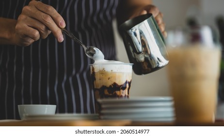 Unrecognizable  Barista Using Spoon To Gentle Topping Glass Of Sweet Coffee At Bar Counter With White Milk Froth From Metal Jar To Enhance Taste Of Softness And Mellowness