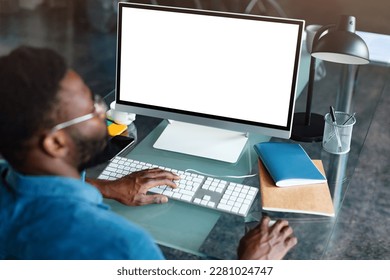 Unrecognizable black businessman using computer with empty blank screen, sitting at workplace in office, offering space for mockup on monitor. Male CEO showing place for online ad