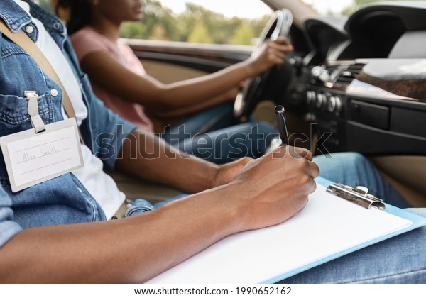 Unrecognizable\
Black Driving Instructor Writing Down Results Of Exam At Chart,\
Closeup. Cropped of african american woman attending driving\
school, passing test, cropped, side\
view