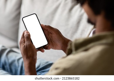 Unrecognizable Black Male Using Smartphone With Blank White Screen At Home, Over Shoulder View Of African American Guy Relaxing On Couch With Empty Mobile Phone, Mockup Image With Copy Space - Shutterstock ID 2123865182