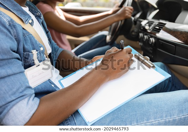 Unrecognizable\
black man driving instructor taking notes at chart during exam,\
closeup. Cropped of african american woman attending driving\
school, passing test, cropped, side\
view