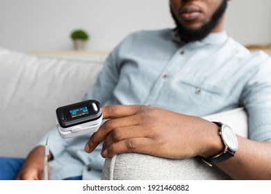 Unrecognizable Black Man With Pulse Oximeter On Hand Measuring Oxygen Saturation Level At Home. Pulseoxymeter Medical Device, Pulseoxymetry Clip Machine Monitorin Ox Rate. Cropped, Selective Focus - Shutterstock ID 1921460882