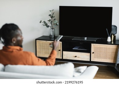 Unrecognizable Black Man Turning On Plasma Flatscreen TV-set, Pointing Remote Control At Empty Black TV Screen, Switching Channels At Home, Mockup