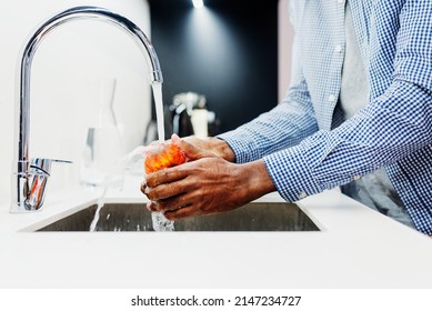 unrecognizable black man's hands washing an apple with tap water in the kitchen. healthy diet concept