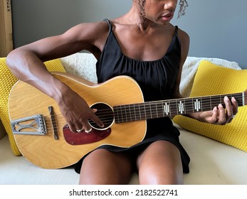 An unrecognizable Black person strumming a guitar on a couch