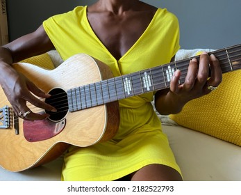 An unrecognizable Black person strumming a guitar on a couch