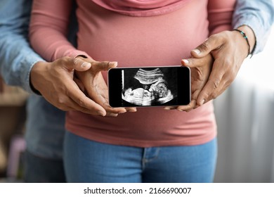 Unrecognizable Black Pregnant Couple Holding Smartphone With Their Baby Sonography Photo, African American Spouses Embracing And Showing Mobile Phone With Child Ultrasound Image On Screen, Cropped